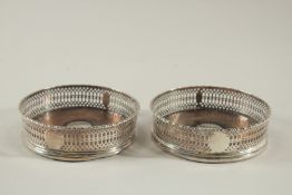 A PAIR OF GEORGE III SILVER CIRCULAR WINE COASTERS with wooden bases. 4.75ins diameter London 1773.