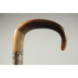 A CURVING RHINO HORN HANDLED WALKING CANE with silver band.