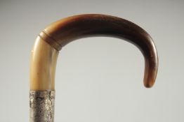 A CURVING RHINO HORN HANDLED WALKING CANE with silver band.