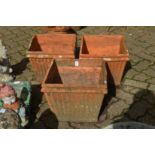 A set of three terracotta square shaped plant pots.