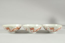 THREE CHINESE COPPER RED AND WHITE PORCELAIN BOWLS, painted with dragons and stylised clouds with