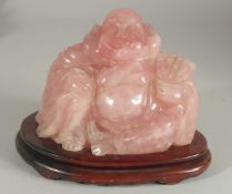A CHINESE CARVED ROSE QUARTZ BUDDHA on wooden stand, 19cm wide overall.