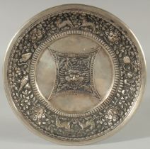 A TIBETAN OR NEPALESE EMBOSSED WHITE METAL DISH, 24cm diameter.