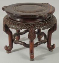 A LARGE CHINESE CARVED HARDWOOD STAND, with circular top, the skirt carved with bat motifs, elevated