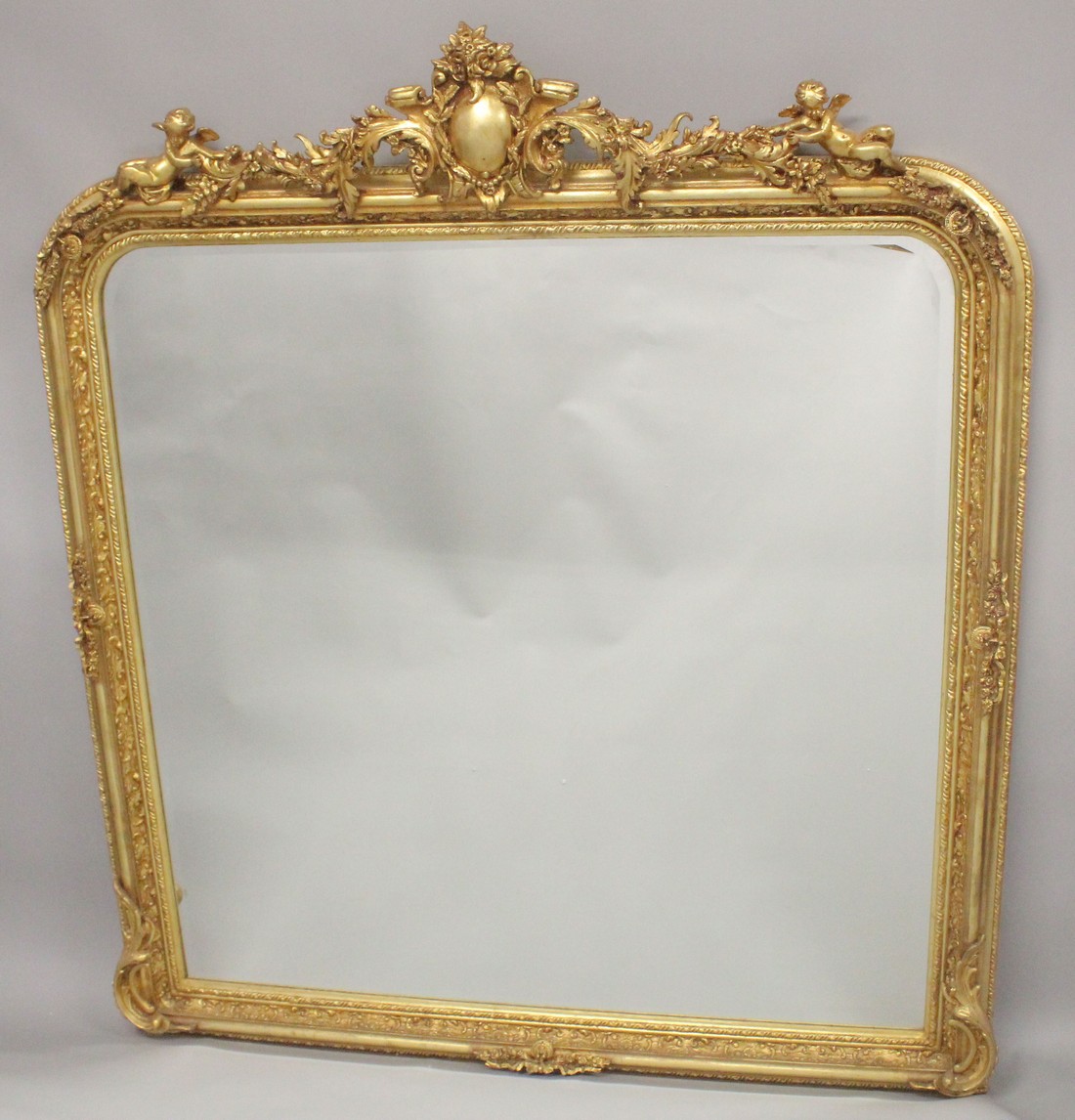 A LARGE GILTWOOD OVER MANTLE MIRROR with scrolls and cupids. 5ft 6ins high, 4ft 8ins wide.