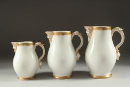 A GARNITURE OF THREE WHITE PORCELAIN GILDED JUGS with mask spouts.
