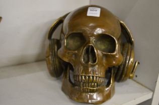 An unusual cast bronze sculpture of a skull wearing headphones.