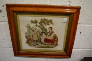 A wool work picture depicting figures under a tree mounted in a maple frame.