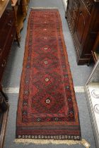 A Persian runner, red ground with stylised decoration 290cm x 70cm.