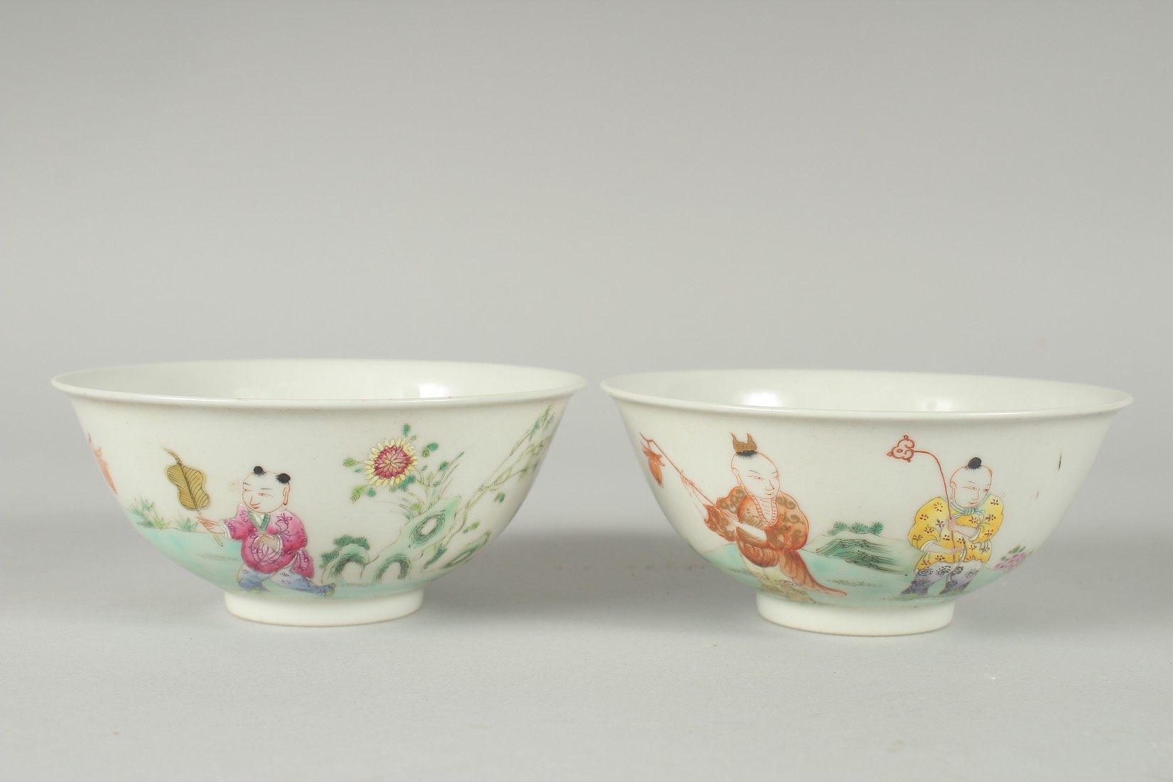 A PAIR OF EARLY 20TH CENTURY FAMILLE ROSE PORCELAIN RICE BOWLS, painted with boys, each with red