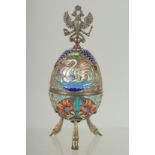 A LARGE RUSSIAN SILVER AND ENAMEL EGG on three curving feet. 12cm long 5cm diameter decorated with