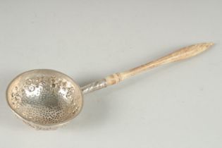 A SMALL WHITE METAL STRAINING SPOON, the rim embossed with fruit and leaves with a turned wood