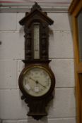 A barometer/thermometer with carved oak frame.