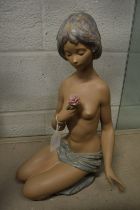 A large Lladro pottery seated semi nude female figure holding a rose in her hand.