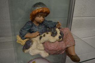 A large Lladro pottery model of a young child seated with a puppy on its lap.