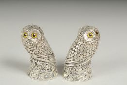 A pair of silver plated owl salt and peppers with yellow eyes.