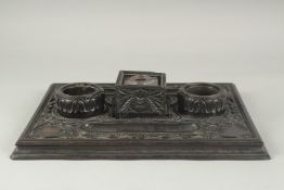 A FINE EARLY 19TH CENTURY CEYLONESE CARVED EBONY DESK INK STAND, with glass inkwell, 36cm x 26cm.