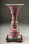 A CHINESE PINK GROUND FAMILLE ROSE PORCELAIN SECTIONAL GU VASE, and fitted hardwood stand, bearing