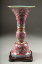A CHINESE PINK GROUND FAMILLE ROSE PORCELAIN SECTIONAL GU VASE, and fitted hardwood stand, bearing