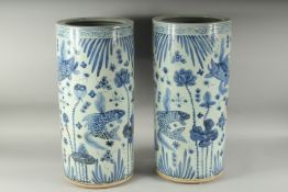 A PAIR OF CHINESE BLUE AND WHITE UMBRELLA STANDS decorated with carp. 23ins high.