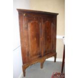 A Georgian carved oak and inlaid corner cupboard enclosed two ogee arch top doors, on later