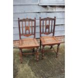 A pair of Chinese carved hardwood vertical rail back dining chairs with panel seats, on shaped