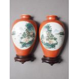 A pair of Chinese wall pockets, formed as vases, decorated panels with landscapes on an orange