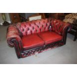 A two-seat chesterfield settee with loose seat cushions, upholstered in a red leather, 64" wide x