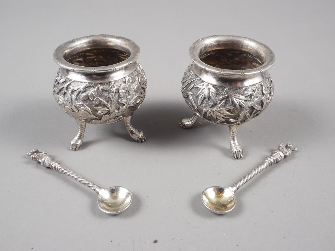 A pair of Chinese white metal salt cellars with engraved figures in a landscape decoration, on three