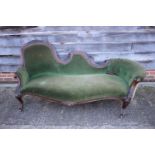 A Victorian carved walnut showframe conversation settee, upholstered in a green velour, on