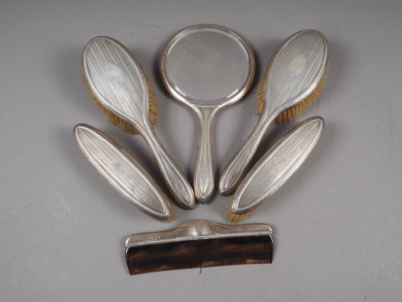 A silver backed dressing table set, comprising four brushes, a comb and a hand mirror