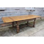 An oak draw leaf dining table, on carved, turned and square supports united by an 'X' stretcher,
