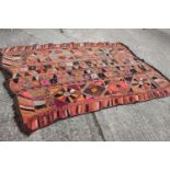 A wool work wall hanging with geometric designs in shades of orange, pink, purple, red, grey and