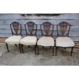 A set of four carved mahogany Sheraton revival standard dining chairs with shield-shaped backs, on