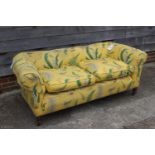 An early 20th century Chesterfield settee, upholstered in a leaf printed yellow linen, on turned and