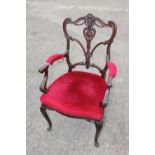 A late 19th century carved walnut open arm chair, upholstered in a red velvet, on cabriole supports