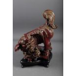 A Chinese red and brown glazed porcelain model of a Dog of Fo, on hardwood stand, 16" high