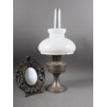 A chrome oil lamp with milk glass shade and a bronze coloured easel back photograph frame