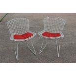 A pair of white painted wire mesh chairs, in the manner of Harry Bertoia, with red seat pads