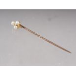 A yellow metal stick pin, mounted three pearls and two diamond brilliants