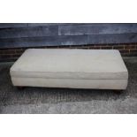 An ottoman, upholstered in fawn moquette, on turned supports, 58" wide x 28" deep x 14" high