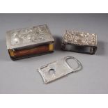 A silver cigar cutter with engraved decoration, a silver matchbox holder, and a similar larger white