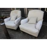 A pair of cream deep seat armchairs with loose cushions, on turned and castored supports