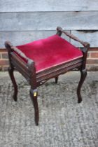 An early 20th century walnut piano stool with box seat upholstered in a red velour, on cabriole