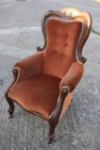 A Victorian carved walnut showframe armchair, upholstered in a rust velour, on cabriole supports