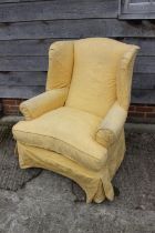 A wing armchair of Georgian design, with down loose seat cushions and yellow loose covers, on square