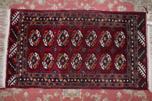 A Bokhara rug with fourteen guls on a plum ground and multi-bordered in shades of black, orange