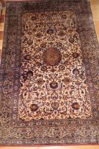A Kashan silk rug with central medallion and all-over foliate scroll design on a light ground and