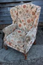 A wing armchair of Georgian design with loose seat cushion, upholstered in a floral fabric, on