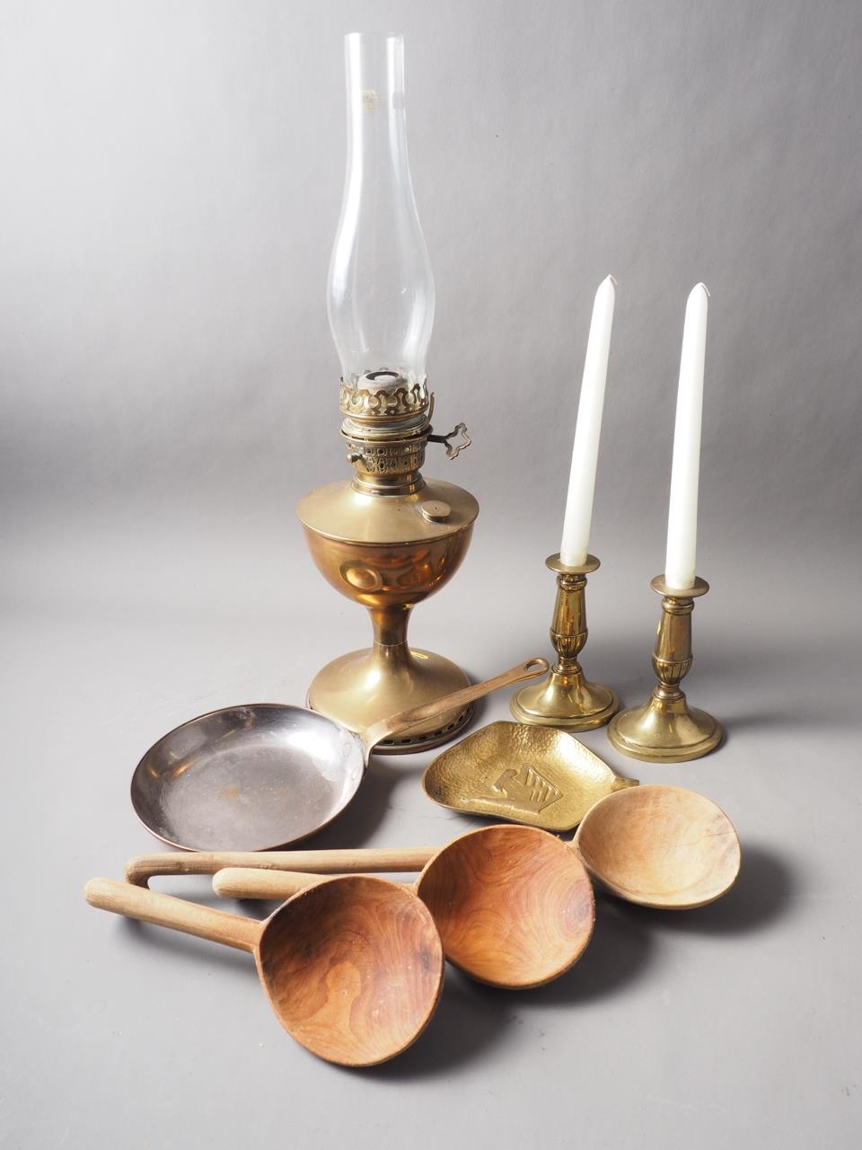 A brass oil lamp, a pair of brass candlesticks, a copper saucepan, a bronze ashtray and three carved
